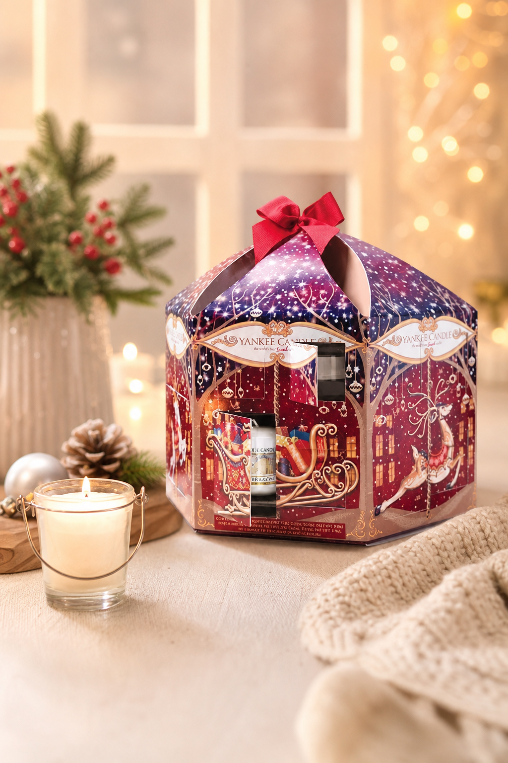 Yankee Candle Adventskalender mit geöffnetem Türchen neben brennender Kerze und Tannenzweig