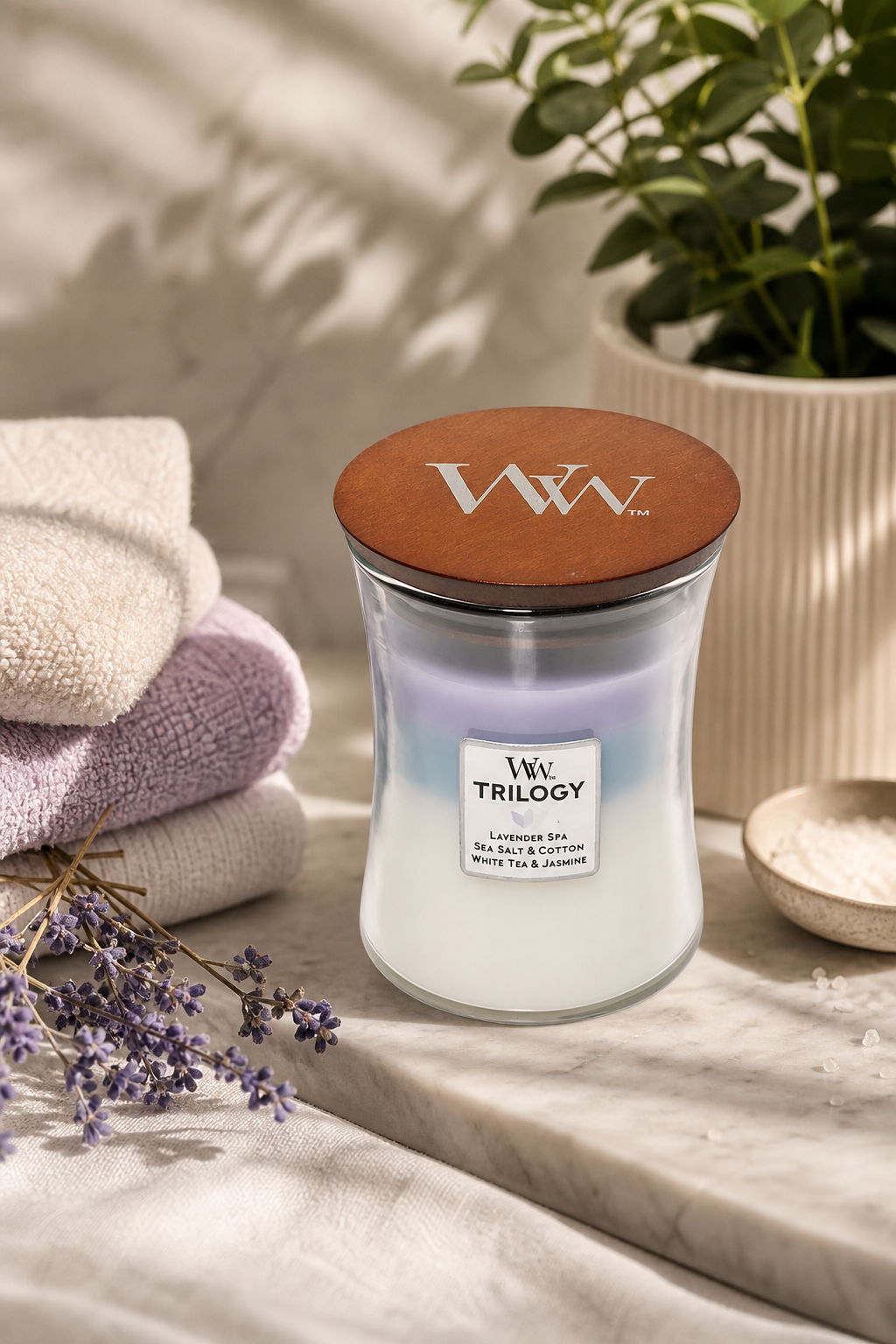 WoodWick Trilogy Kerze mit Holzdeckel neben Handtüchern und Lavendel