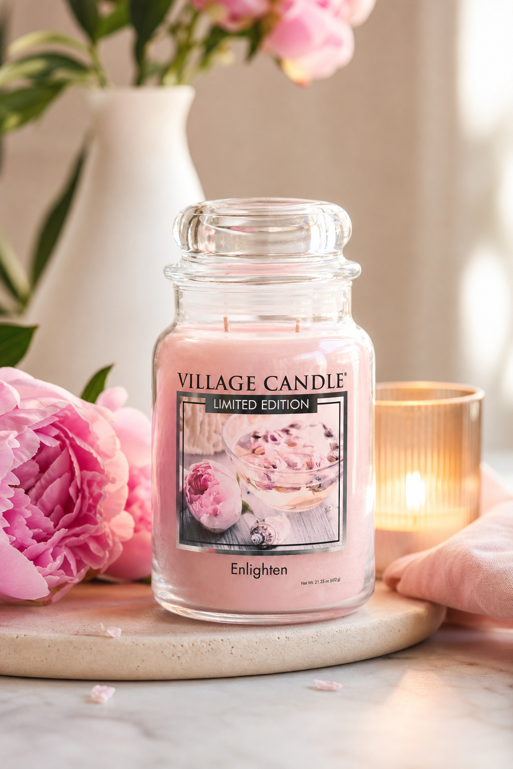 Village Candle Enlighten Kerze auf Ablage neben Blumen und brennender Kerze