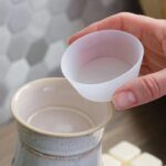 Hand hält eine weiße Schale über einem keramischen Wachswärmer