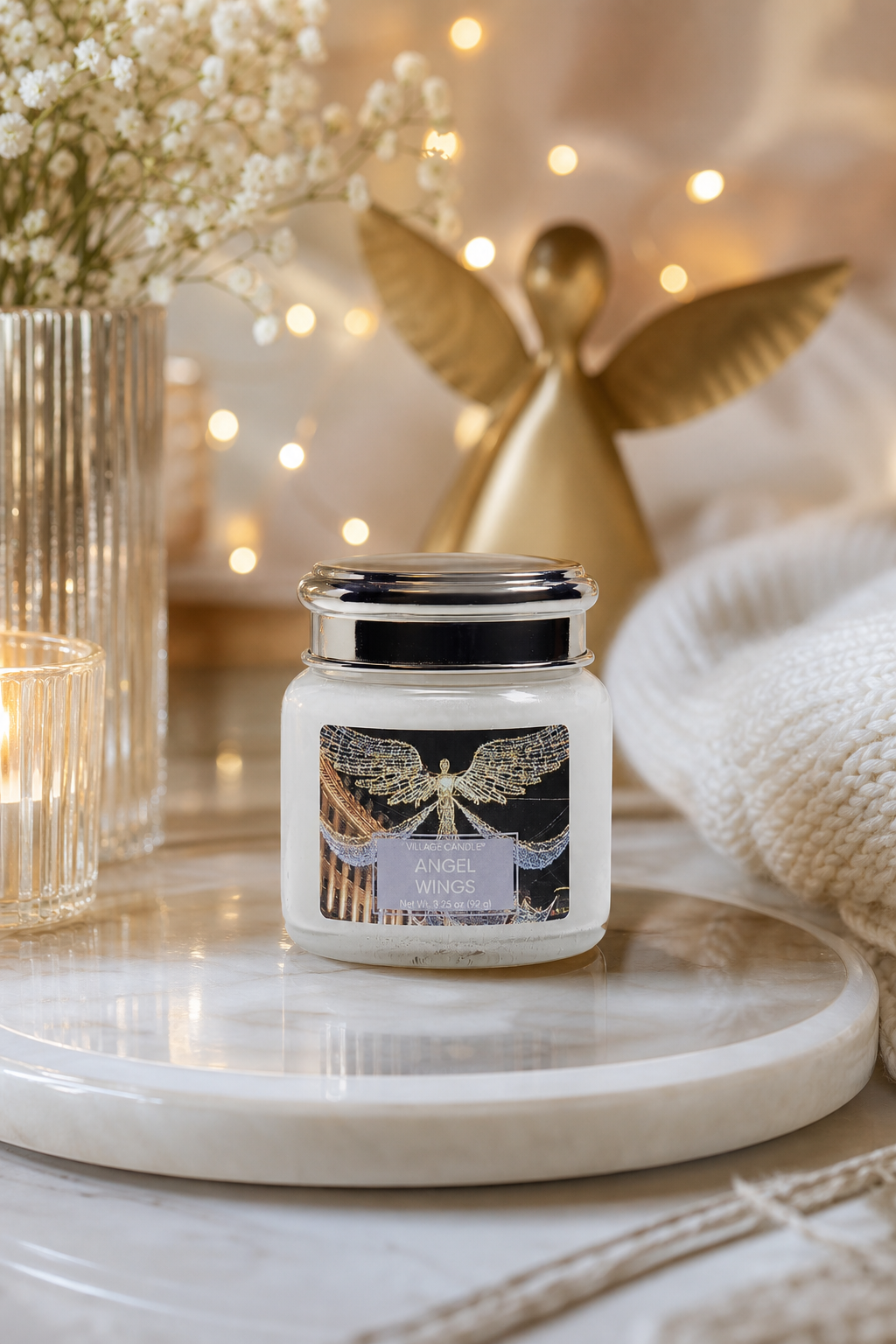 Angel Wings Kerze auf einer weißen Platte vor einer Engelsfigur und Lichterkette