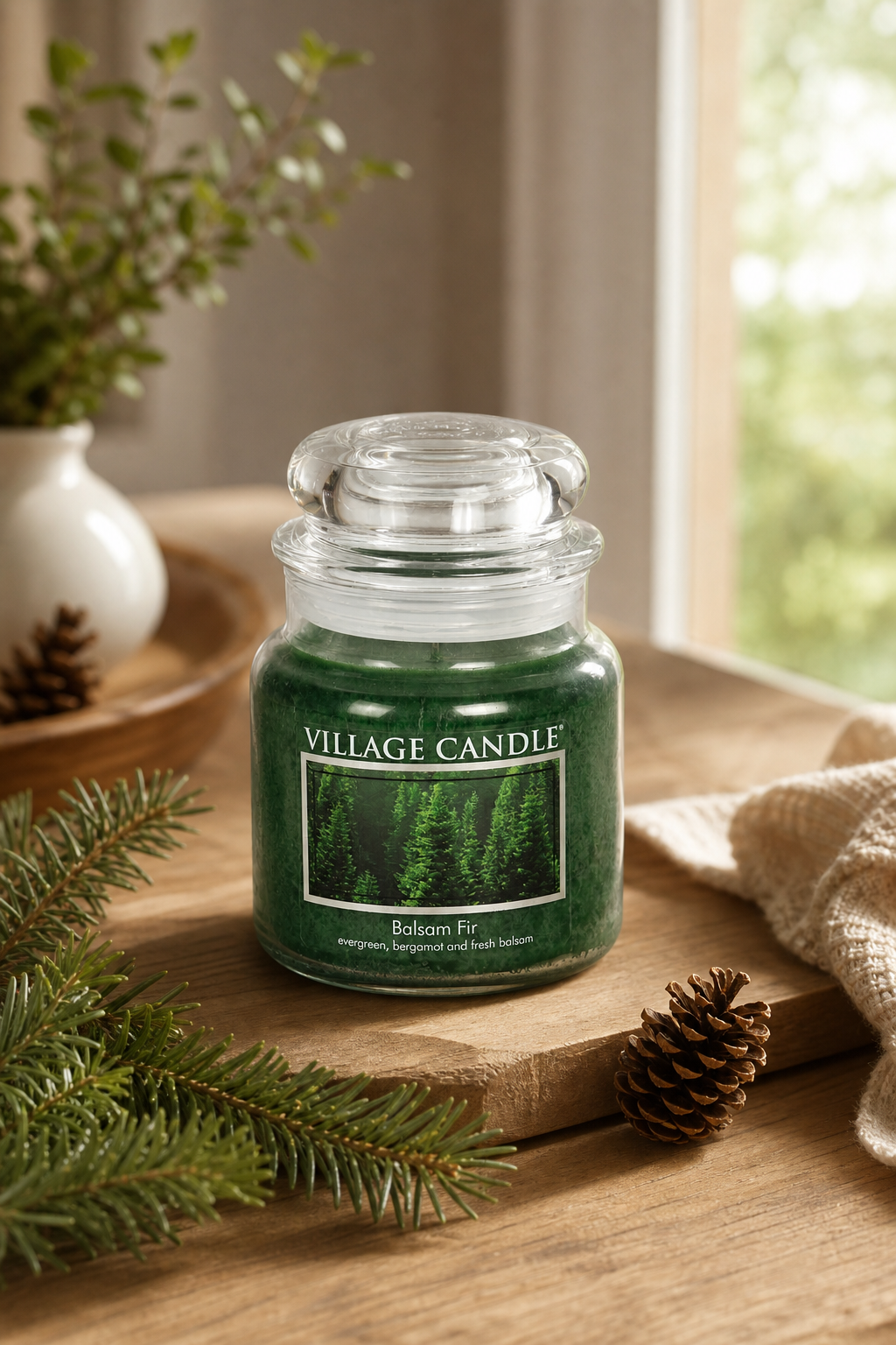 Grüne Village Candle Balsam Fir steht auf einem Holztisch neben Tannenzweigen