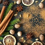 Zimtstangen, Sternanis, Muskatnüsse und Orangenscheiben auf dunkler Fläche