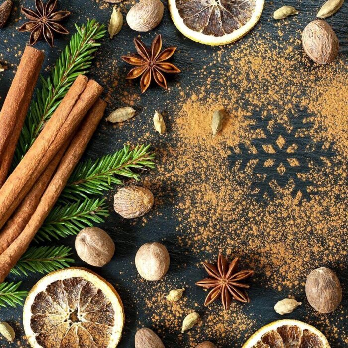 Zimtstangen, Sternanis, Muskatnüsse und Orangenscheiben auf dunkler Fläche