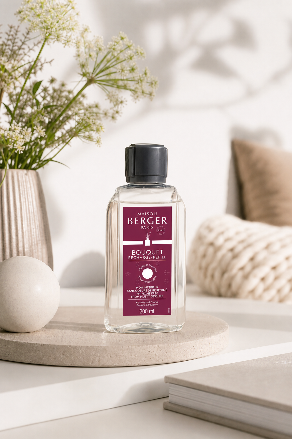 Maison Berger Paris Nachfüller steht auf einem Tisch neben Vase und Kissen