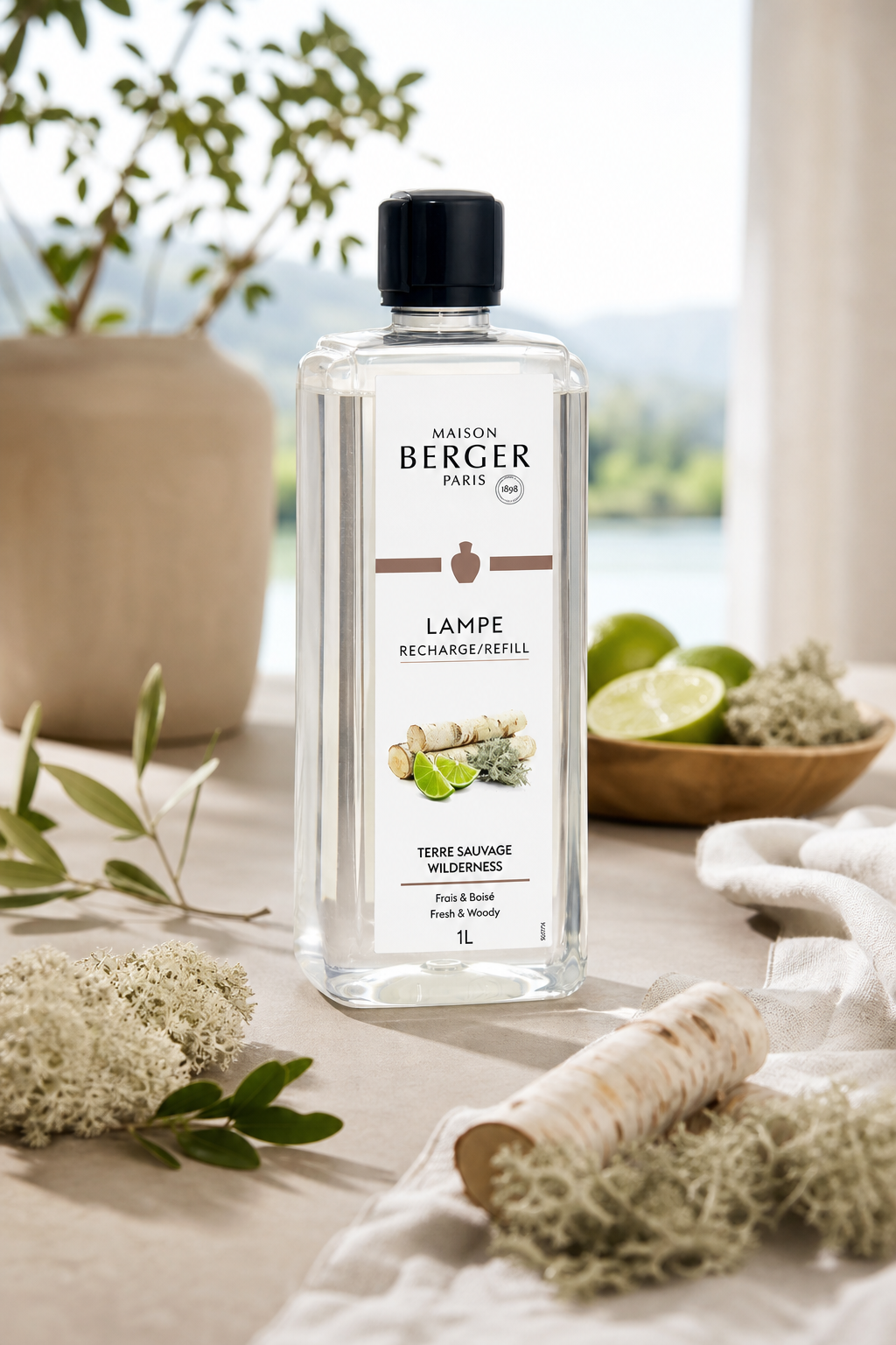Maison Berger Lampen-Nachfüllflasche Terre Sauvage auf einem Tisch neben Limetten und Pflanzen