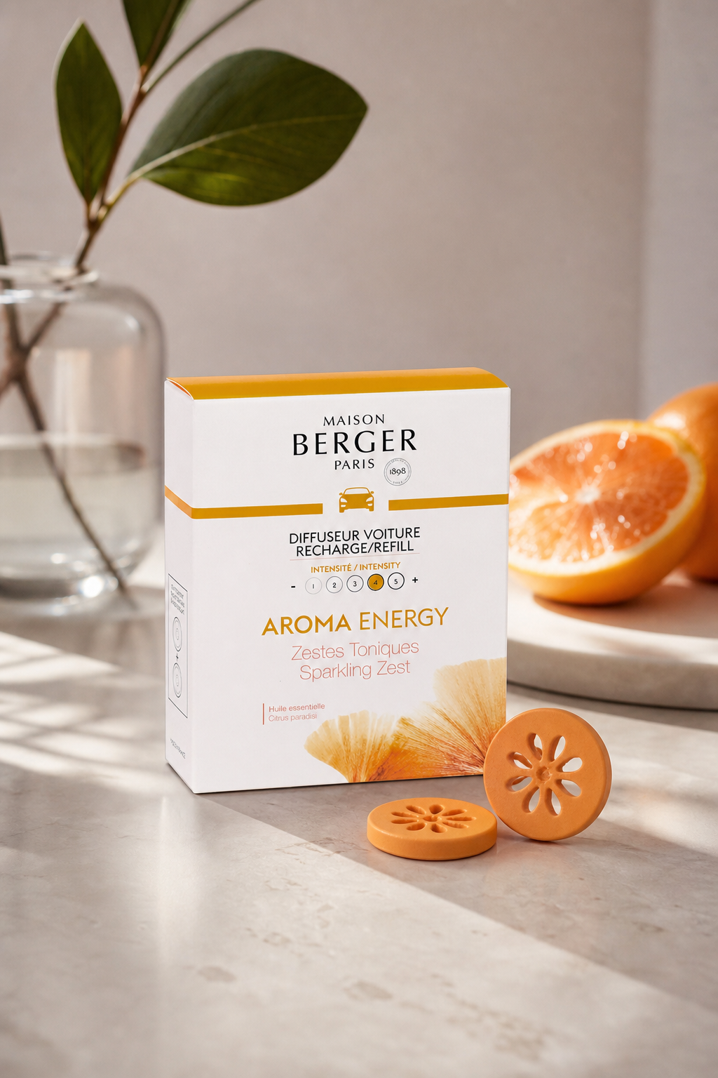 Aroma-Energy-Verpackung neben orangefarbenen Duftobjekten und halbierter Orange