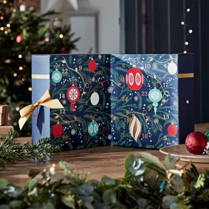 Geöffneter Adventskalender mit nummerierten Türchen vor Weihnachtsbaum und Dekoration
