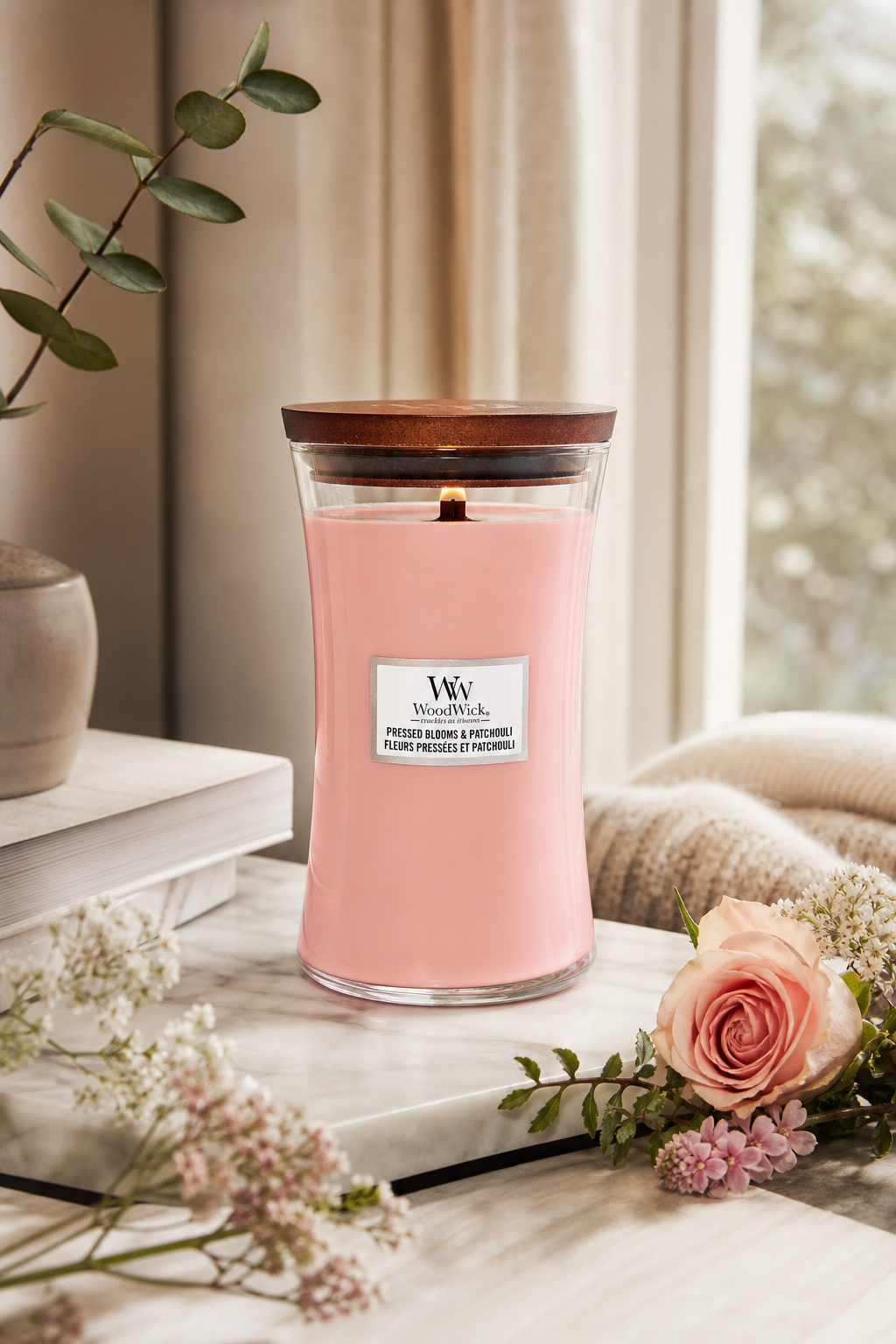 WoodWick Kerze mit rosa Wachs auf Tisch neben Blumen und Fenster