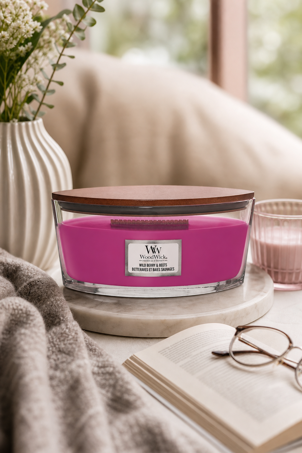 WoodWick Wild Berry & Beets Kerze auf Tisch neben Buch und Decke