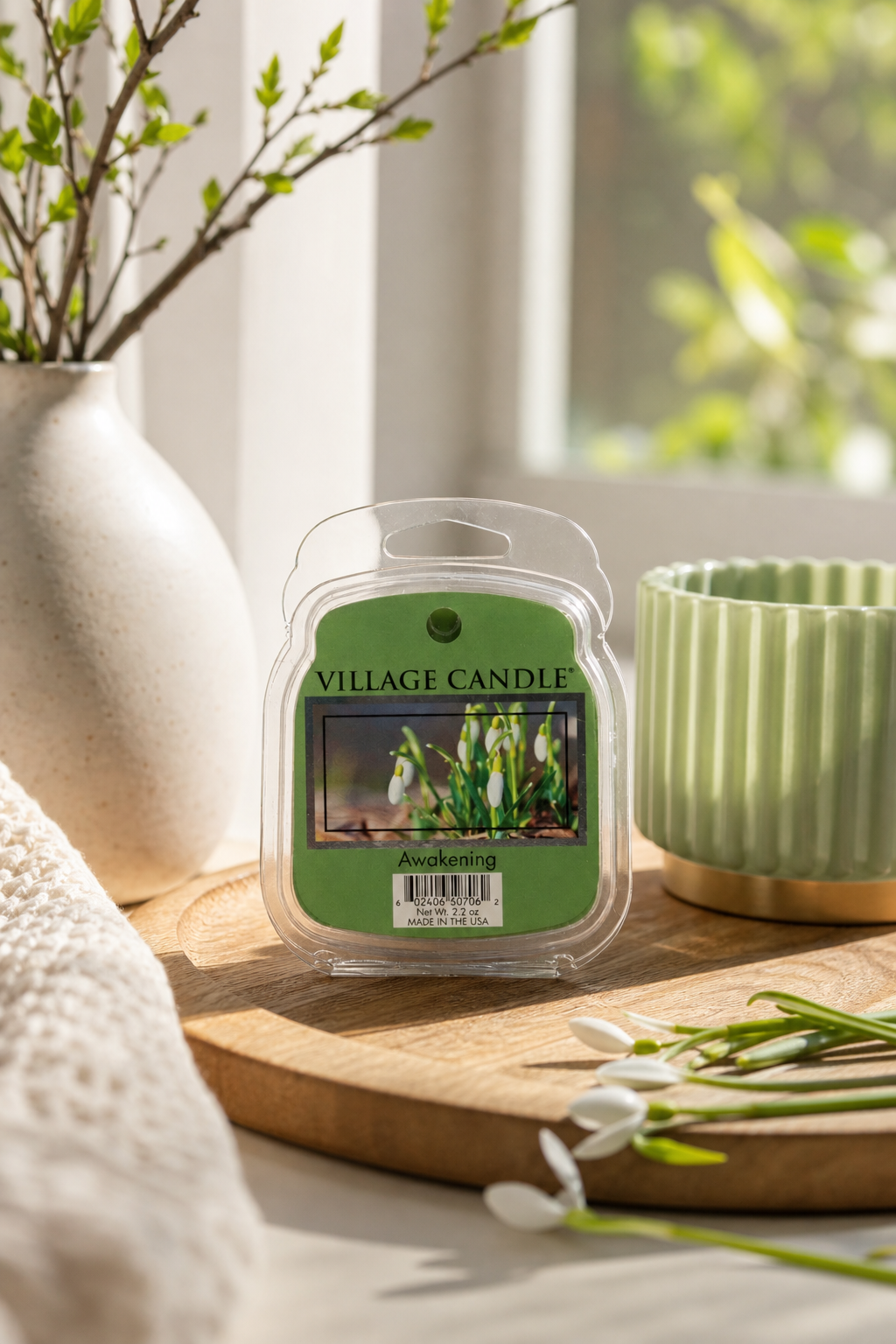 Verpacktes Village Candle Awakening steht auf einem Holztisch neben Vase und Becher