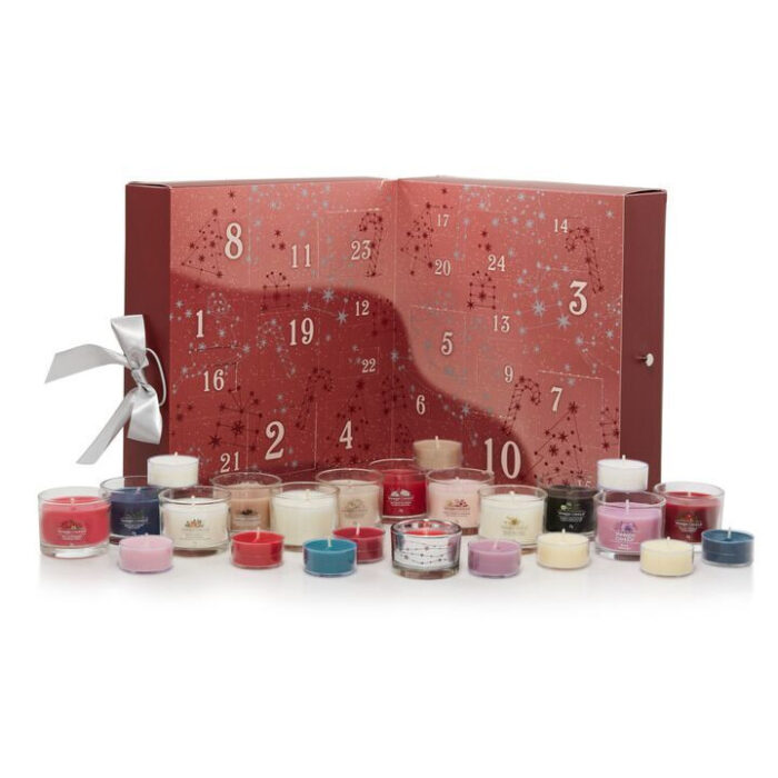 Geöffneter Adventskalender mit kleinen Kerzen vor einem Weihnachtsbaum