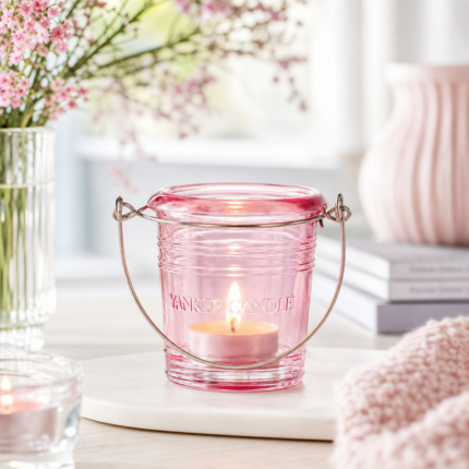 Rosa Yankee Candle Laternengefäß mit brennender Kerze auf einem weißen Buch