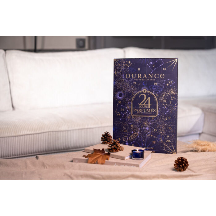 Durance Adventskalender neben einer brennenden Duftkerze und Tannenzapfen