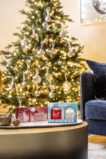 Zwei Yankee Candle Geschenkboxen stehen vor einem beleuchteten Weihnachtsbaum