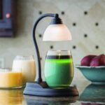 Schwarzer Kerzenwärmer beleuchtet ein grünes Glasgefäß auf einem Tisch