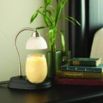 Kerzenwärmer mit leuchtendem Glasgefäß neben Pflanze und Büchern