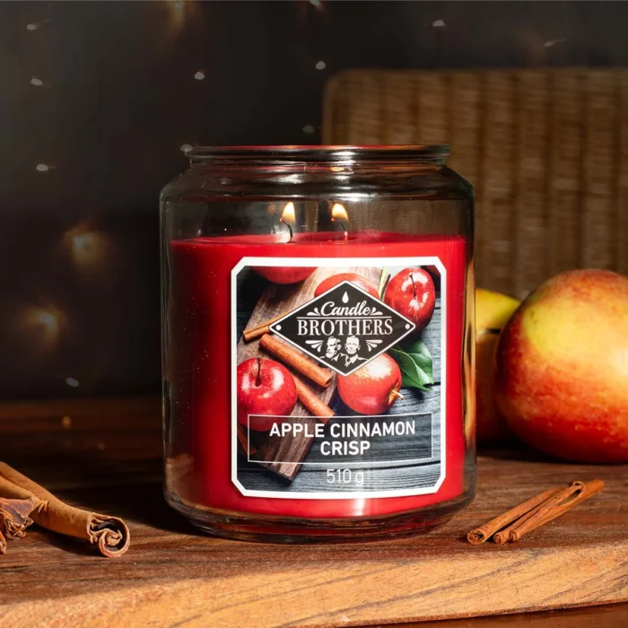 Brennende rote Candle Brothers Kerze mit zwei Flammen neben Äpfeln und Zimt