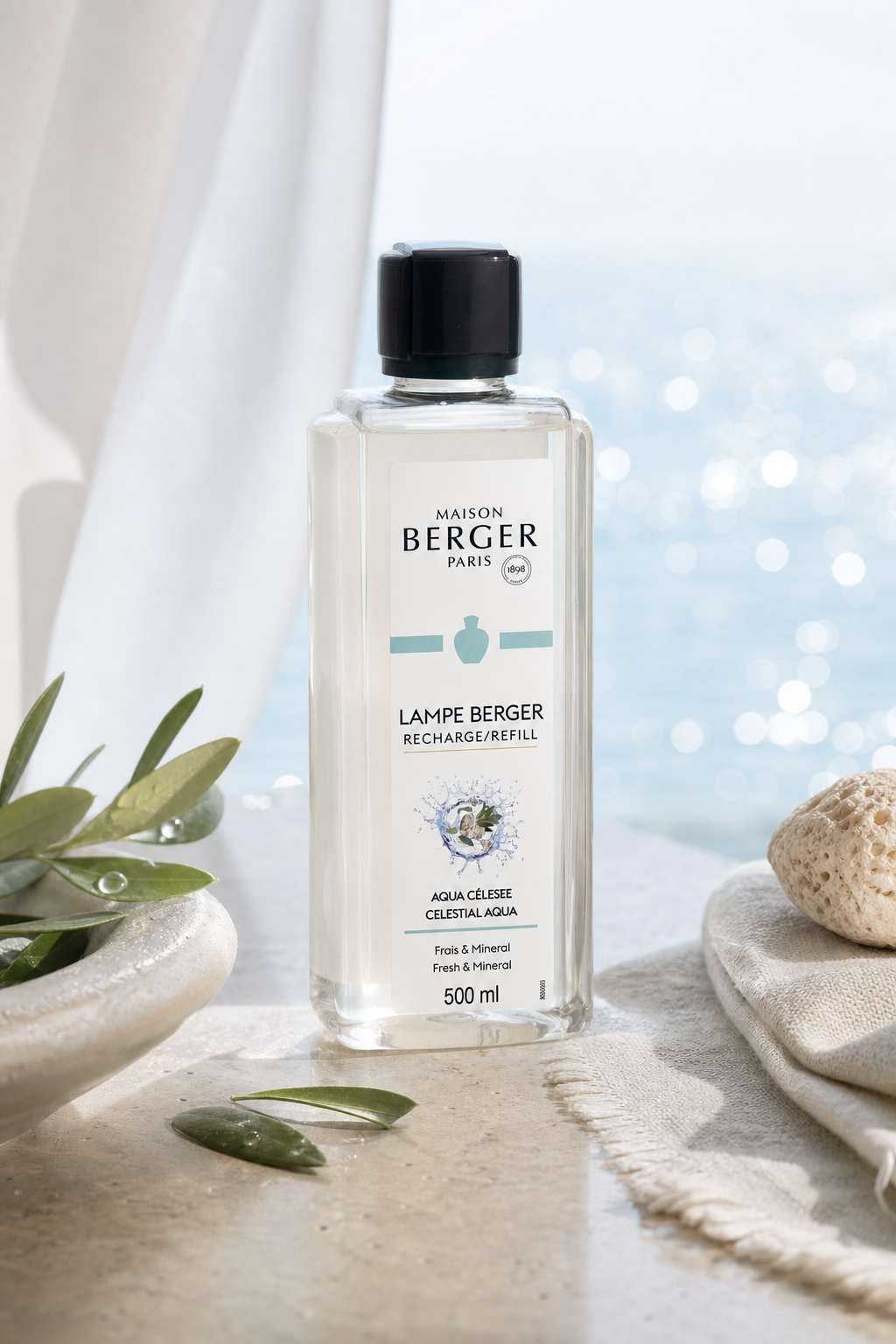 Aqua Céleste Nachfüller auf Steinsockel neben Olivenzweigen und Muscheln