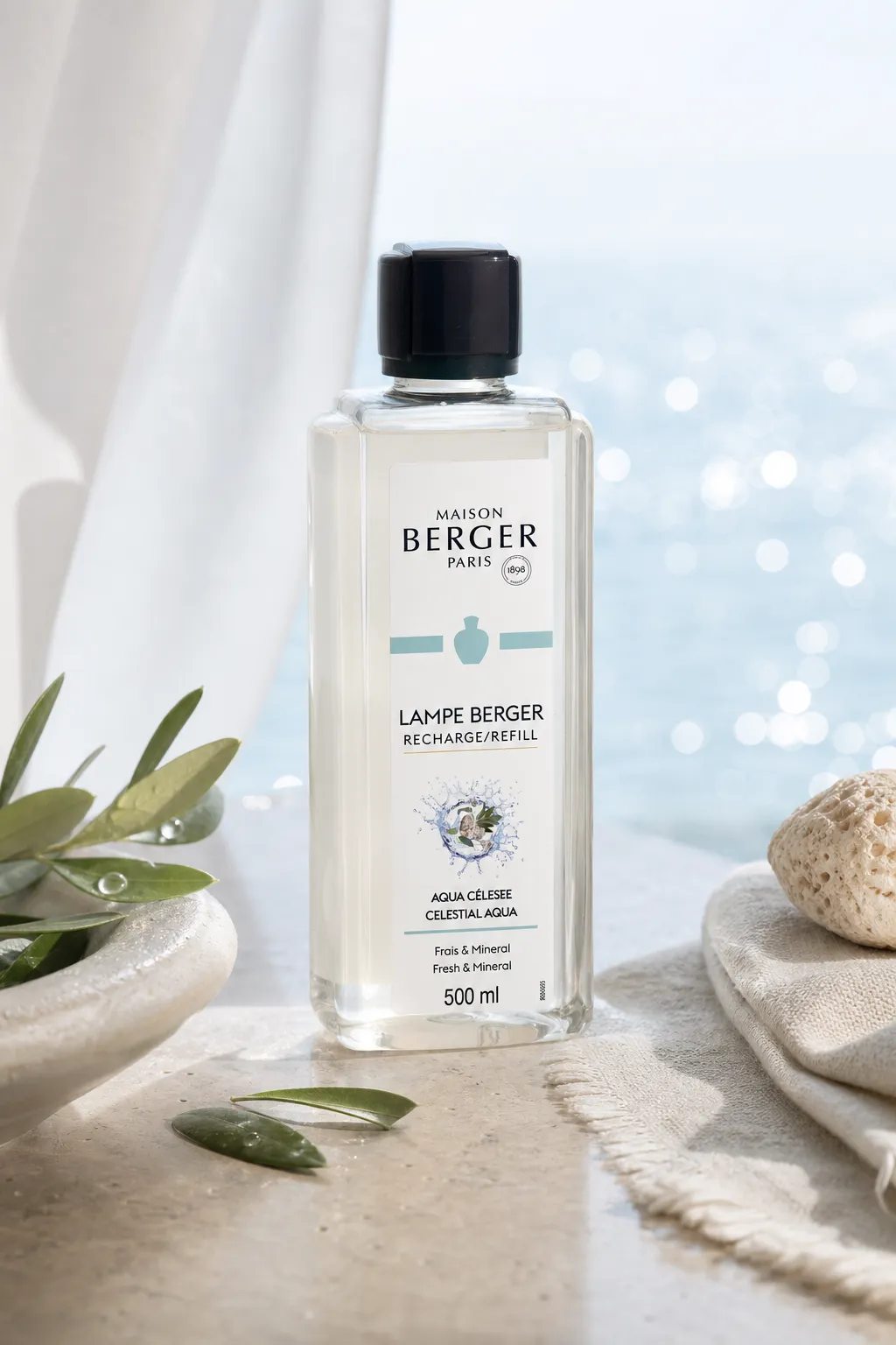 Aqua Céleste Nachfüller auf Steinsockel neben Olivenzweigen und Muscheln