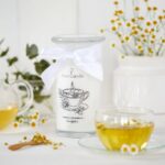 JewelCandle Kerze mit Etikett Aromatic Chamomile & Eucalyptus neben Kamillentee