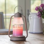 BEACON Laterne mit leuchtender Kerze vor Fenster und Blumen