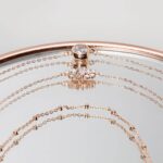 Roségoldfarbene Schmuckarmbänder mit Anhängern auf Spiegeloberfläche