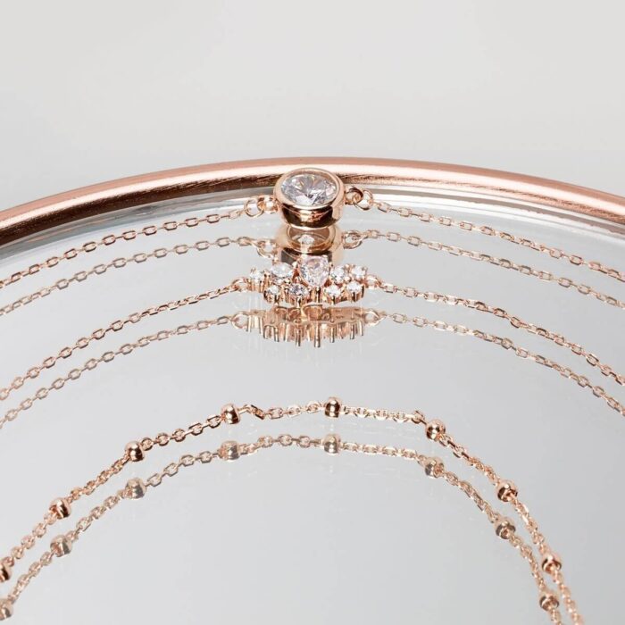 Roségoldfarbene Schmuckarmbänder mit Anhängern auf Spiegeloberfläche