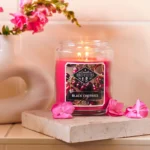 Brennende Black Cherries Kerze im Glas auf einem Podest mit Blumen