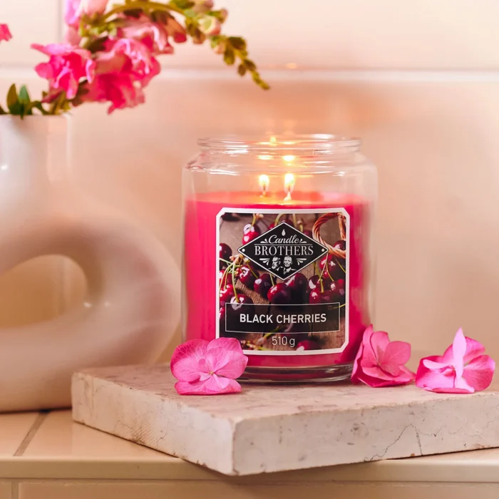 Brennende Black Cherries Kerze im Glas auf einem Podest mit Blumen
