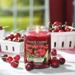 Brennende Black Cherry Kerze neben Kirschen und Beerenschalen