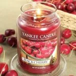 Nahaufnahme einer brennenden Black Cherry Kerze mit Kirschen im Hintergrund
