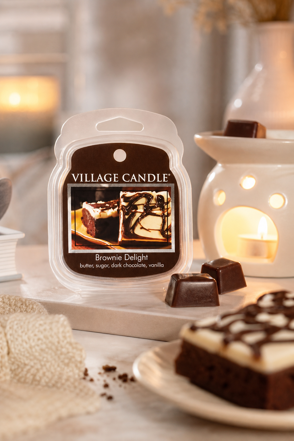 Village Candle Brownie Delight Packung neben Schokolade und brennenden Kerzen