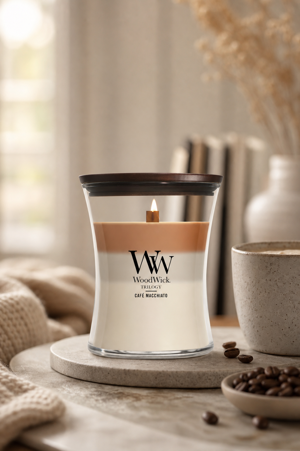 Brennende WoodWick Café Macchiato Trilogy Kerze neben Tasse und Kaffeebohnen