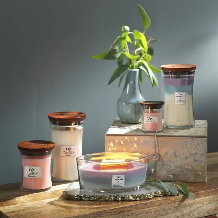 WoodWick Trilogy Kerze mit Deckel neben weiteren brennenden Kerzen
