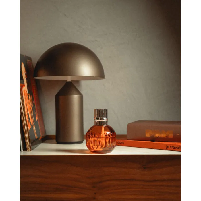 Orangefarbene Lampe Berger mit silberfarbenem Aufsatz auf einem Regal