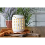 Weiße Duftlampe mit Lochmuster auf einem Holztisch neben einer Topfpflanze