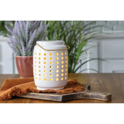 Weiße Duftlampe mit Lochmuster auf einem Holztisch neben einer Topfpflanze