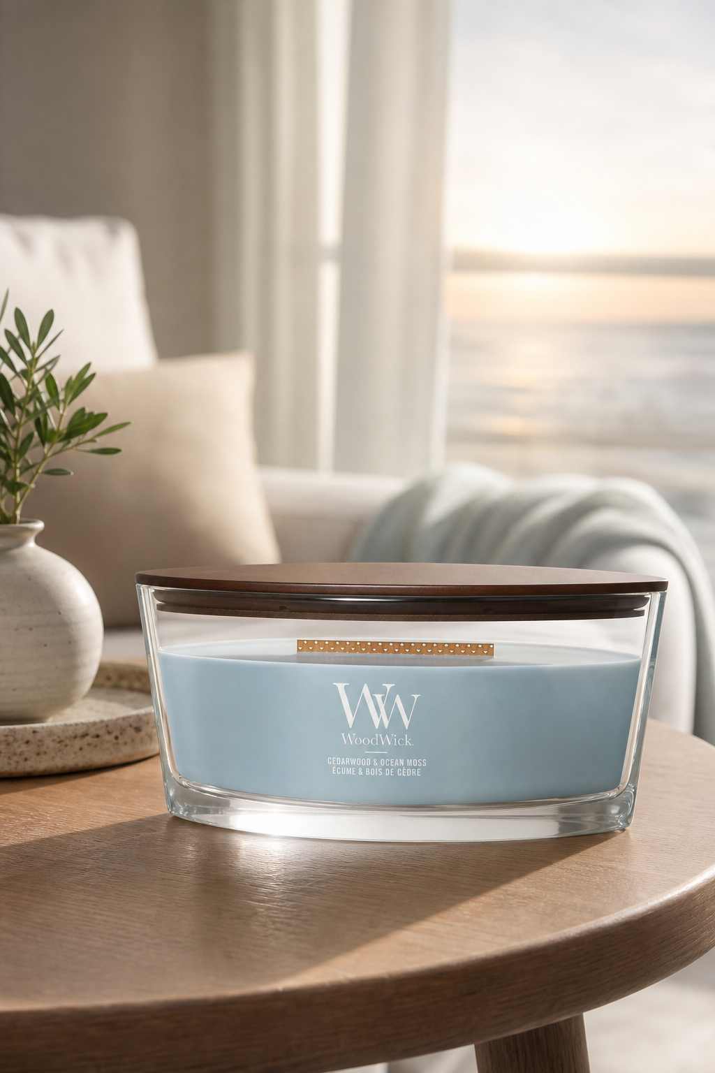 WoodWick Cedarwood & Ocean Moss Duftkerze auf einem Holztisch am Fenster