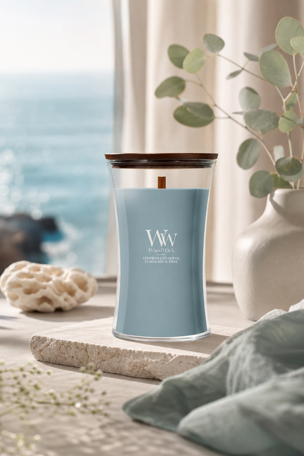 WoodWick Cedarwood & Ocean Moss Kerze auf einem Tisch neben Vase und Meerblick