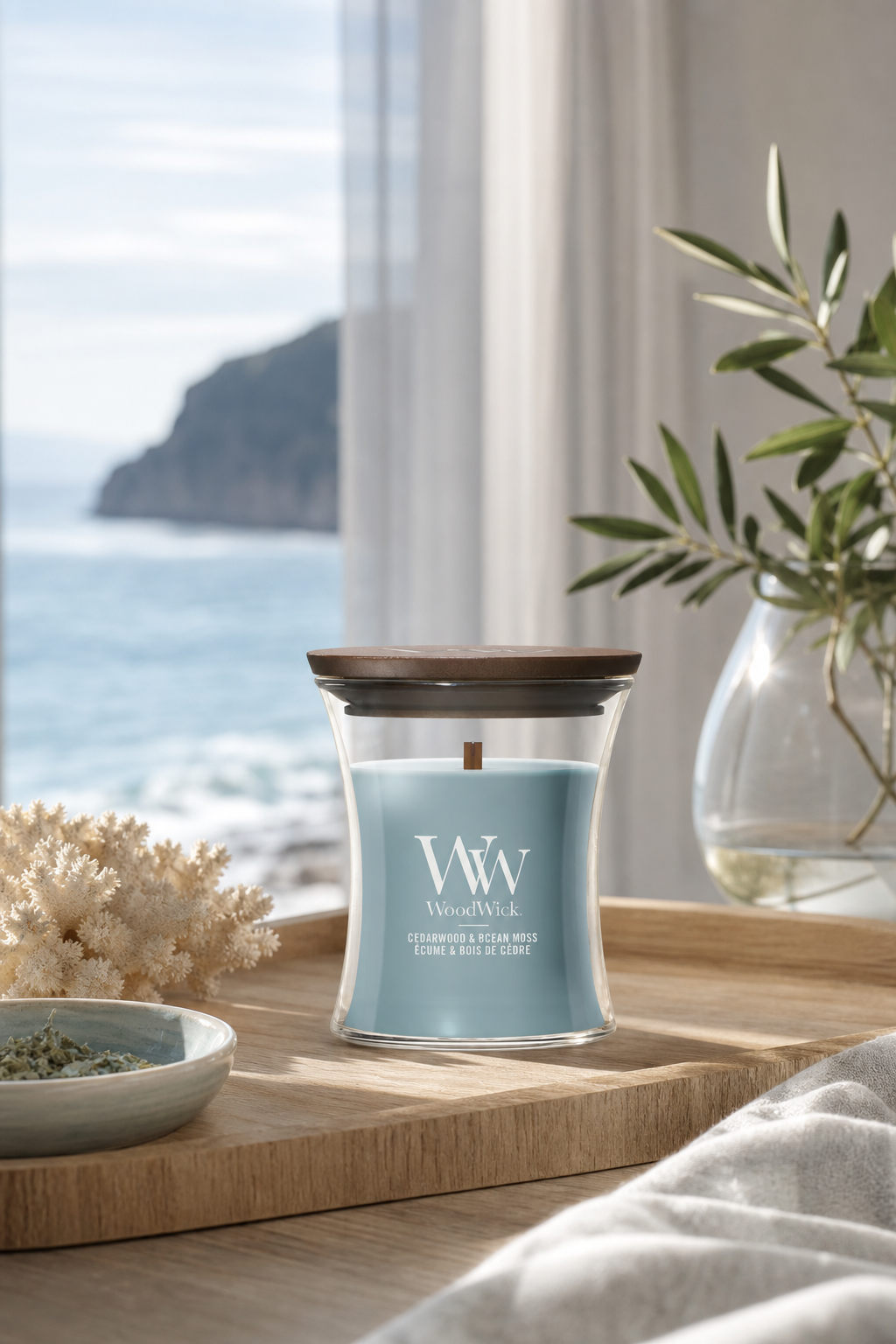 WoodWick Cedarwood & Ocean Moss Kerze mit Holzdeckel auf einem Holztisch am Fenster