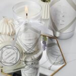 Brennende Charming Kerze neben Verpackung und Schmuck auf einem Tisch