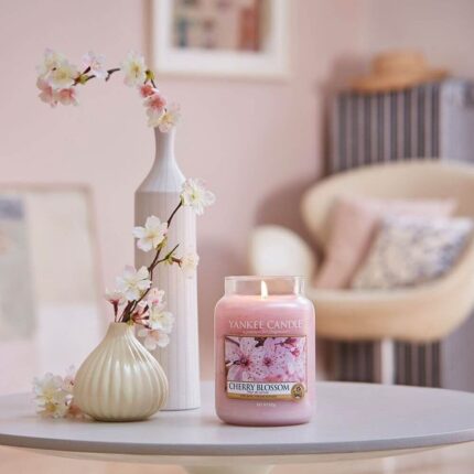 Brennende Cherry-Blossom-Kerze auf Tisch neben Blumenvasen