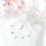 Silberfarbene Kette mit Anhänger neben Kerze und Kirschblüten