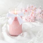 Brennende rosa Kerze im Glas mit weißer Schleife und Kirschblütenmotiv