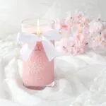 Brennende rosa Kerze im Glas mit weißer Schleife und Kirschblütenmotiv