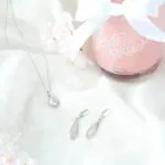 Rosa Kerze mit Schleife neben Kette und zwei länglichen Ohrringen