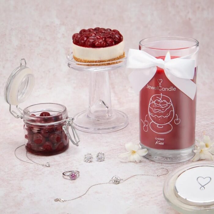 Cherry Kiss Kerze neben Schmuck, Kirschglas und Kirschkuchen
