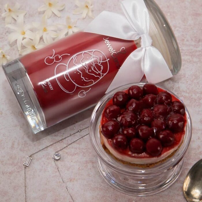 Cherry Kiss Kerze liegt neben Kirschkuchen, Kirschen und Schmuck