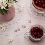 Schmuckstücke und Kette neben Kirschglas, Blumen und Kirschkuchen